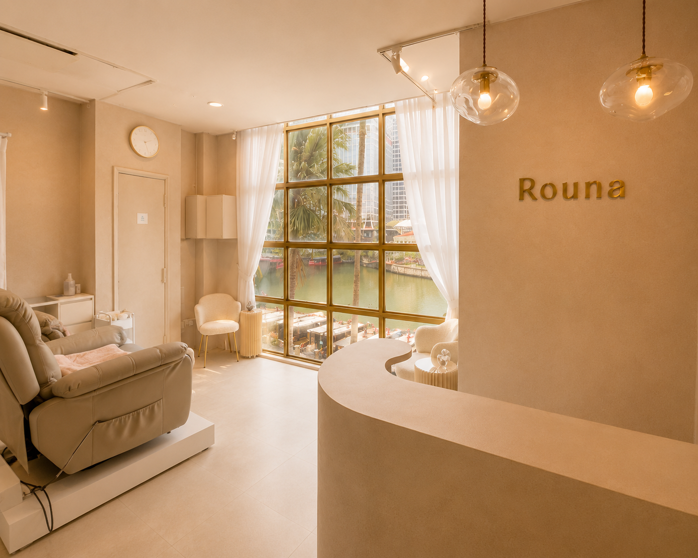 Interior of a wellness or spa lounge with a large window overlooking palm trees and water, featuring cream-colored furniture, a sofa, chairs, curtains, and a wall with the word 'Rouna' displayed.