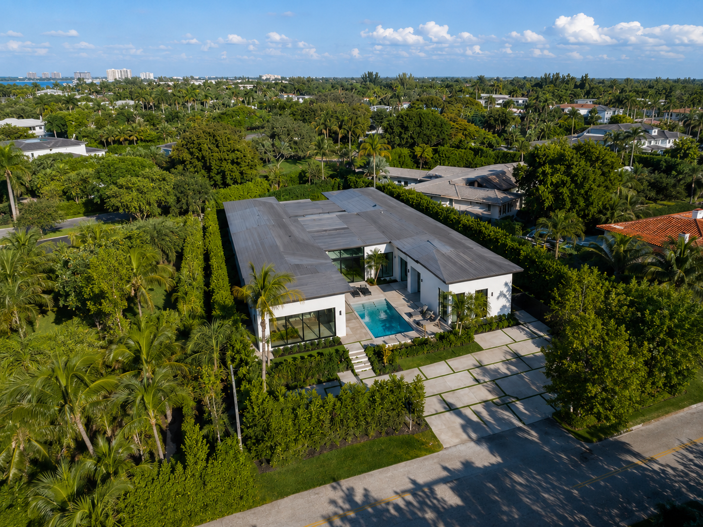 Aerial view of a modern house with a swimming pool, surrounded by lush green trees and landscaped yard.
