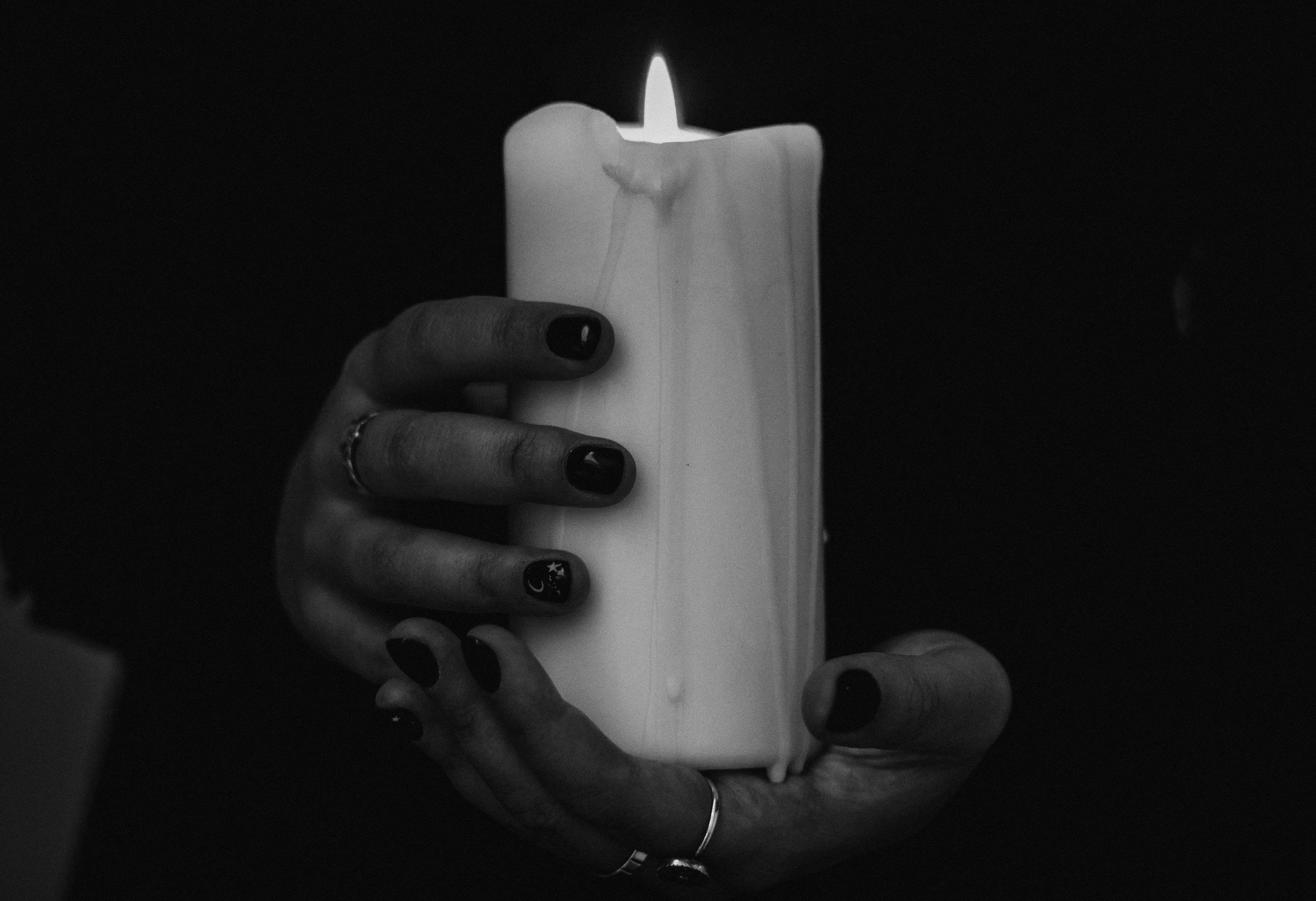 A person with dark painted fingernails holding a lit candle