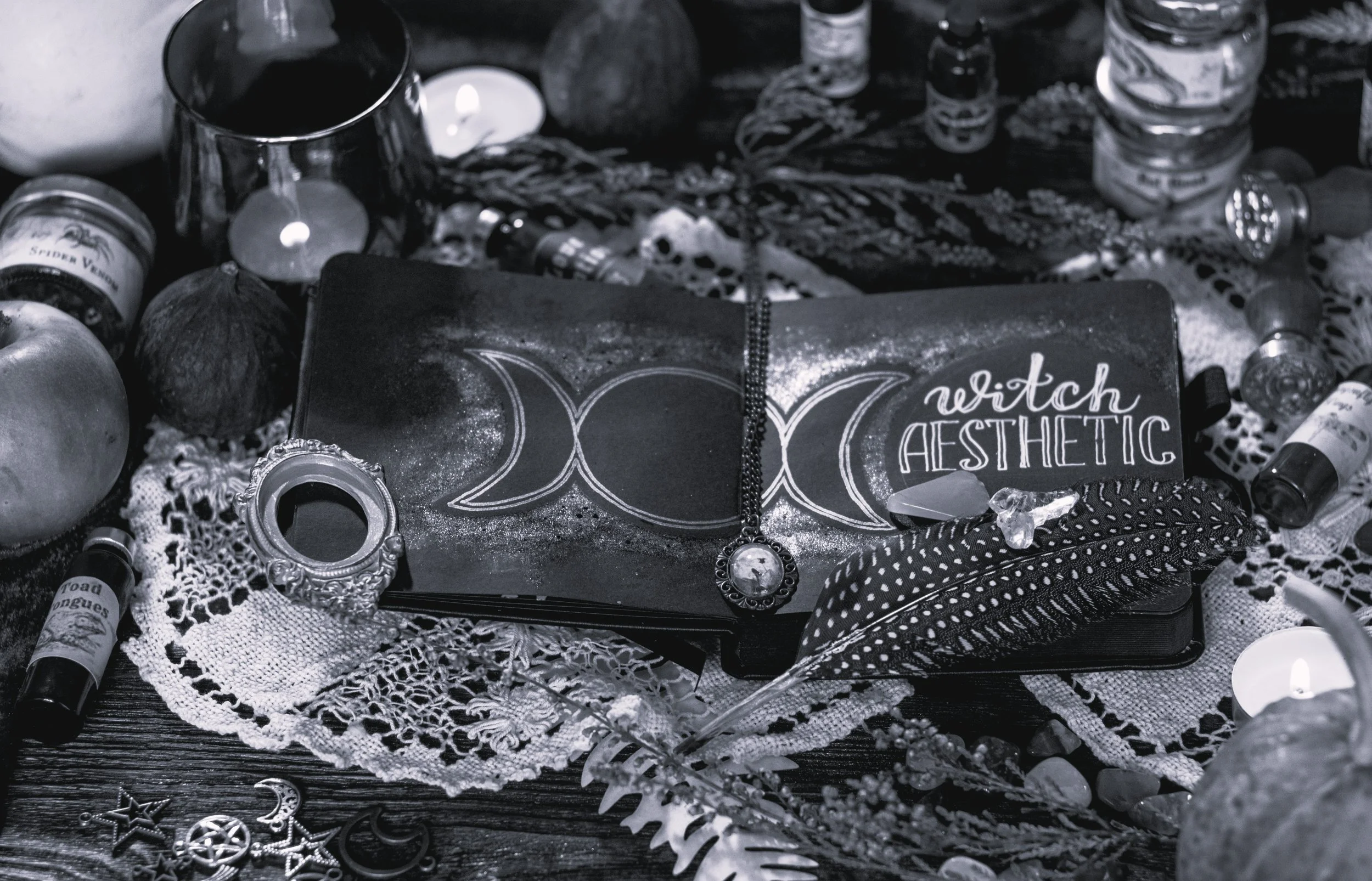 A cluttered table with various objects including jewelry, candles, small jars, and decorative items, with a black box labeled 'witch Aesthetic' and a lace cloth underneath.