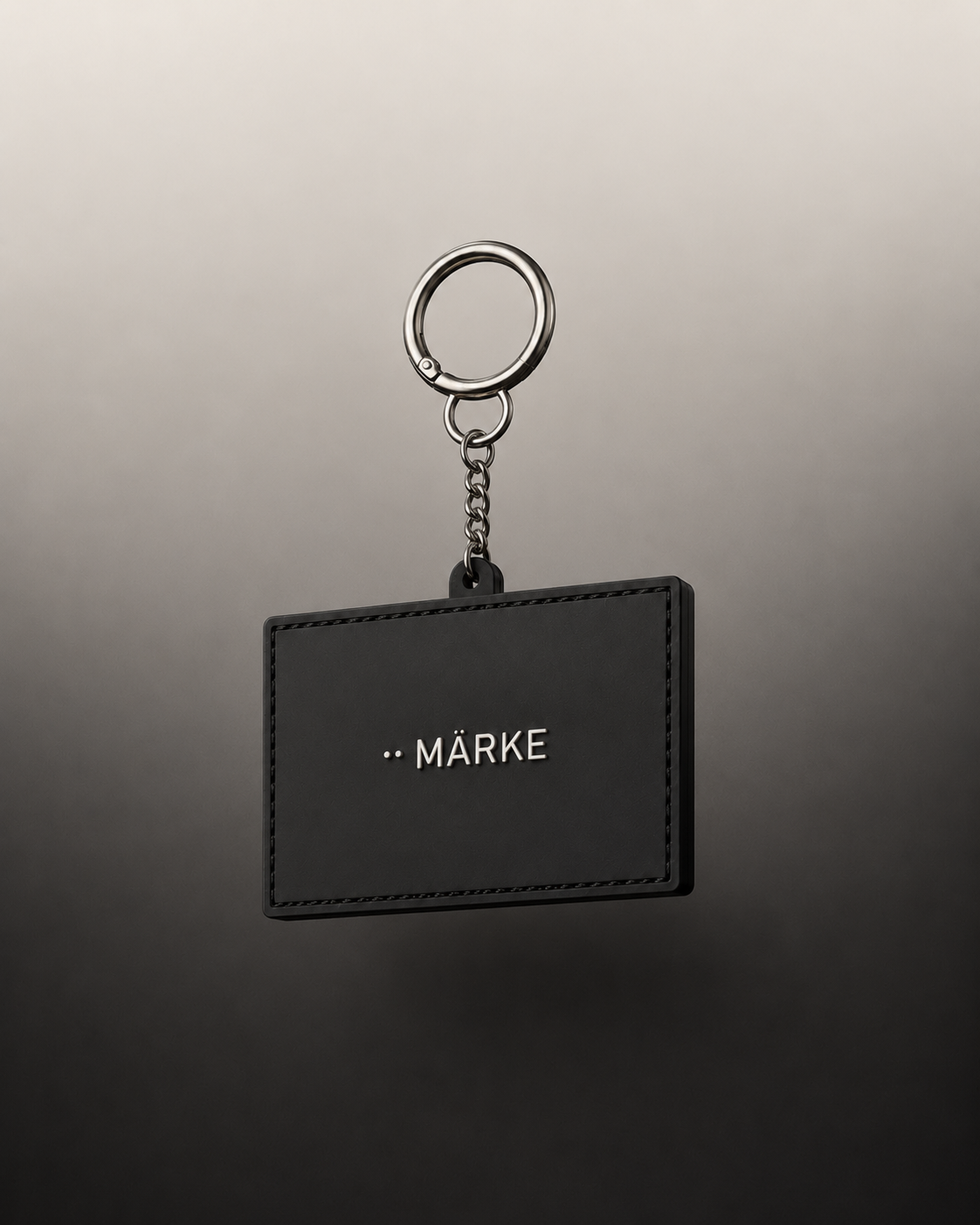 Black keychain holder with the word "MÄRKE" printed on it, hanging from a silver ring and chain
