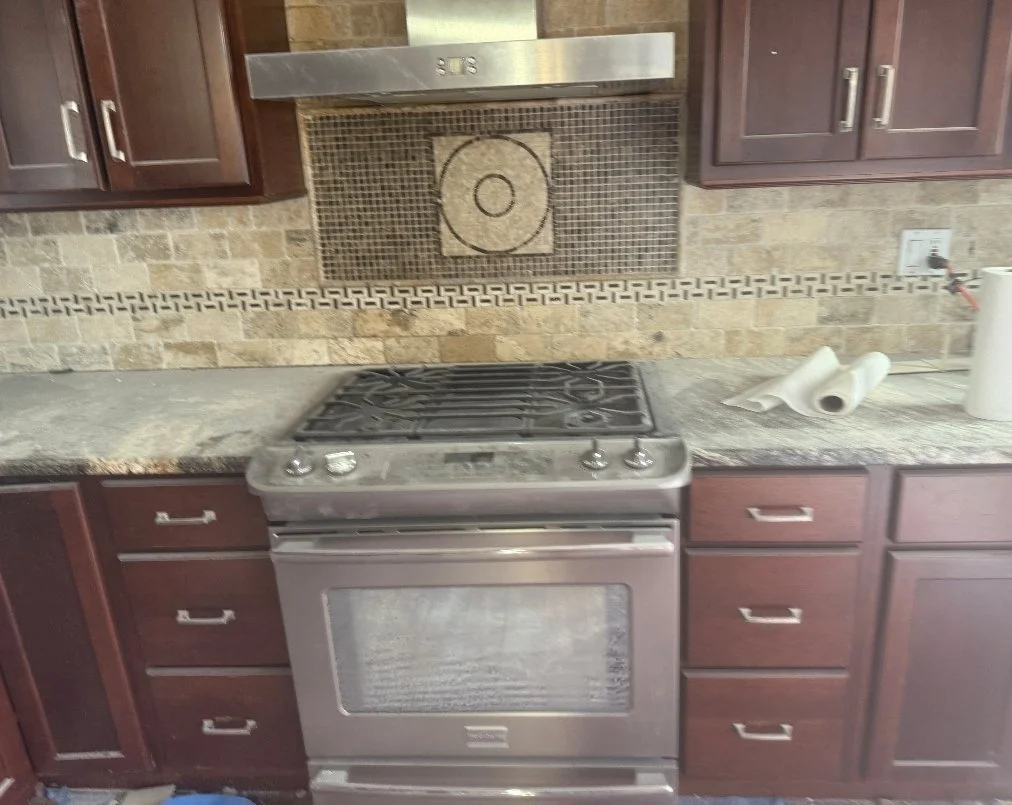 Kitchen with a stove, wooden cabinets, granite countertop, and a tiled backsplash. Paper towels on the right side of the counter.