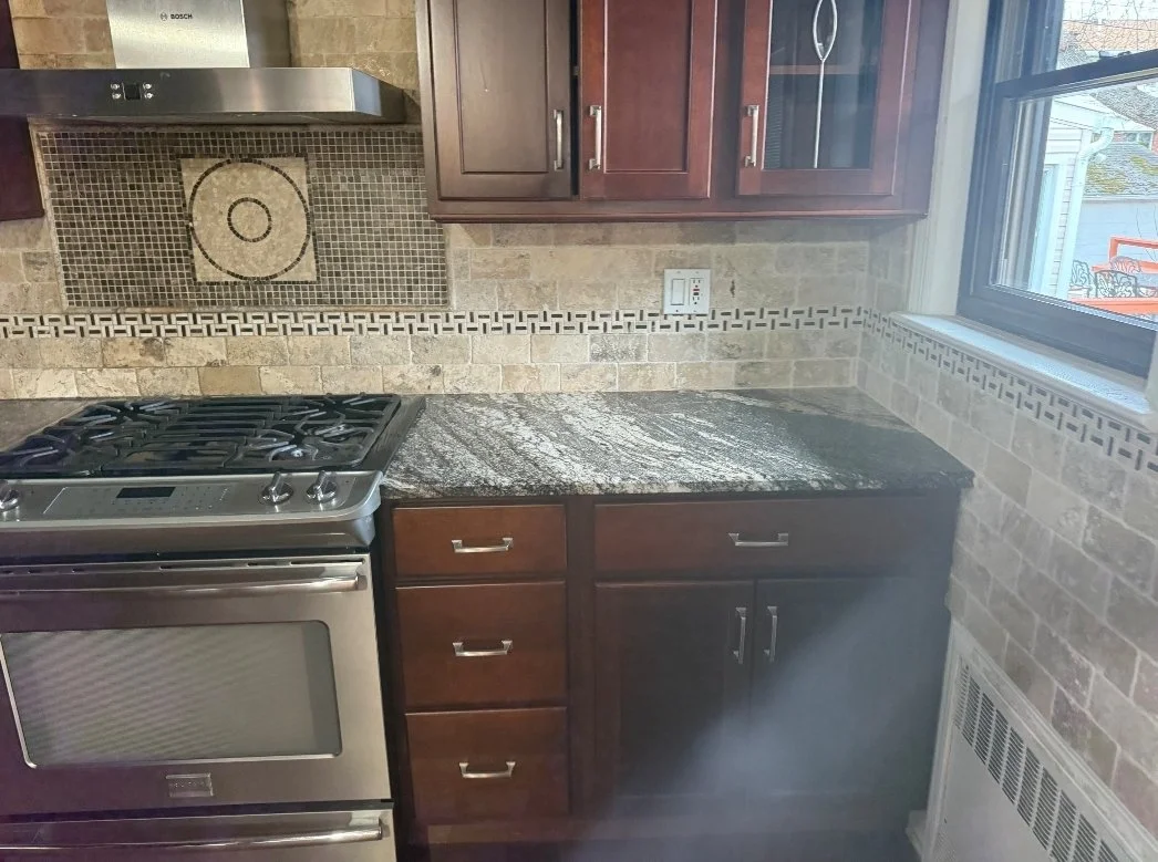 Kitchen with a stove, granite countertop, wood cabinets, and a window to the outside.