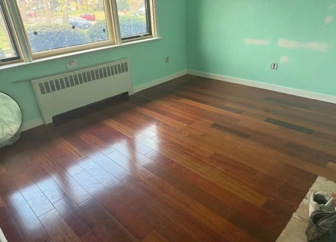 Empty room with green walls, hardwood flooring, large windows, and a wall heater.