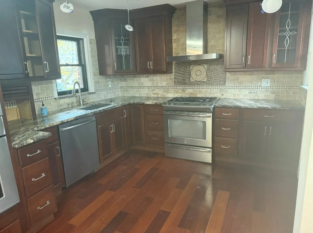 Kitchen with dark wooden cabinets, granite countertops, stainless steel stove and dishwasher, brick backsplash, and hardwood flooring.