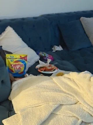 A cozy living room couch with various snacks and a blanket.