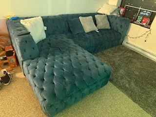 A blue velvet sectional sofa with tufted cushions and several throw pillows in a living room.