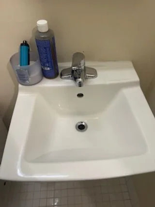 Bathroom sink with a faucet, a bottle of lotion, and a toothbrush holder containing a toothbrush and a blue razer.