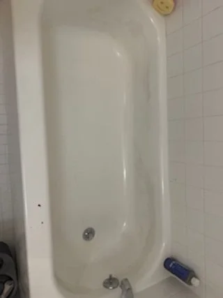 Empty bathtub in a bathroom with white tile walls and some toiletries on the edges.