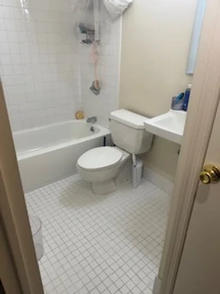Small bathroom with a bathtub, toilet, and sink, with a shower curtain and various toiletries.