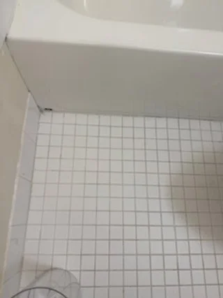 The corner of a bathroom with white tiled floor and a white bathtub or wall panel.