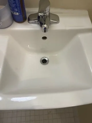 A white bathroom sink with a chrome faucet, soap bottles on the side, and a drain in the center.