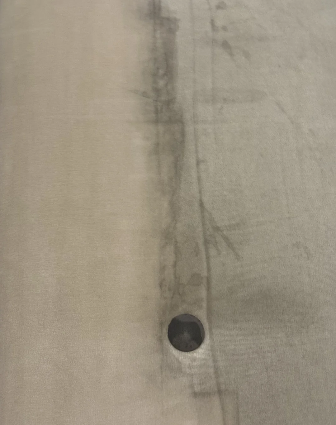Close-up of a beige fabric with a black button and visible stitching.