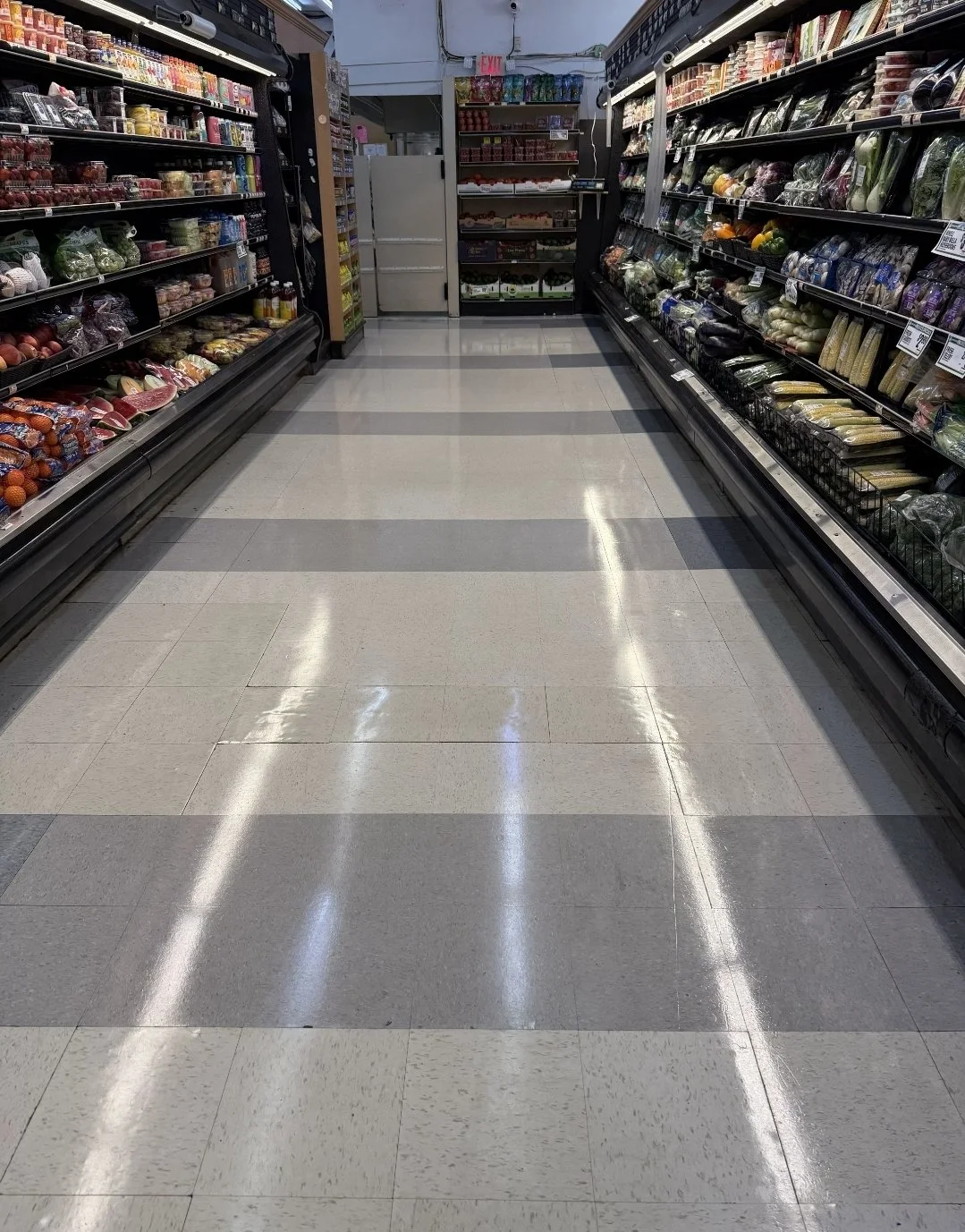 Empty grocery store aisle with shelves stocked with fruits and vegetables on both sides.