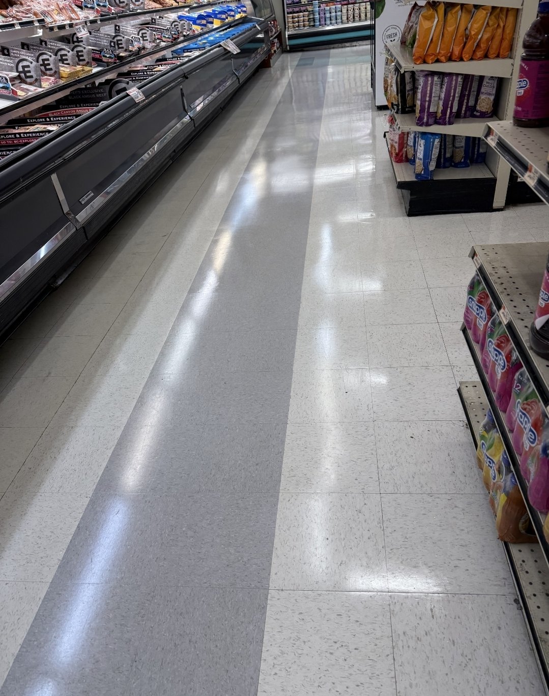 Empty grocery store aisle with shelves on the right stocked with snacks and chips, and a refrigerated section on the left with meat and dairy products.