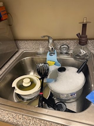 Kitchen sink filled with dirty dishes and utensils, including a pot, a frying pan, a cutting board, a spatula, and a kettle.