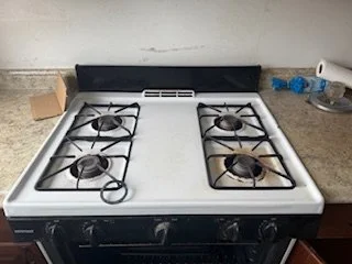 White and black gas stove with four burners, two of which have pots on them, in a kitchen setting.