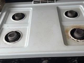 Close-up of a white stovetop with four black burners, some showing signs of rust and wear.