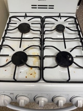 Four burner gas stove with black grates and control knobs, some food spills on the stove surface.