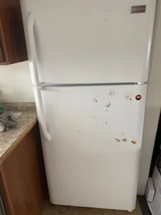 White top-freezer refrigerator with visible stains and a handle on the left side, situated beside a kitchen countertop.
