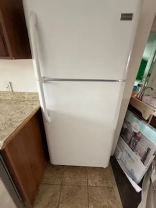 White refrigerator in a kitchen with wooden cabinets and a granite countertop.