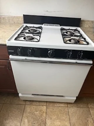White gas stove with four burners and black control knobs in a kitchen.