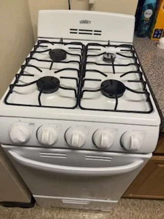 A white gas stove with four burners and control knobs, with an oven door below, in a kitchen.