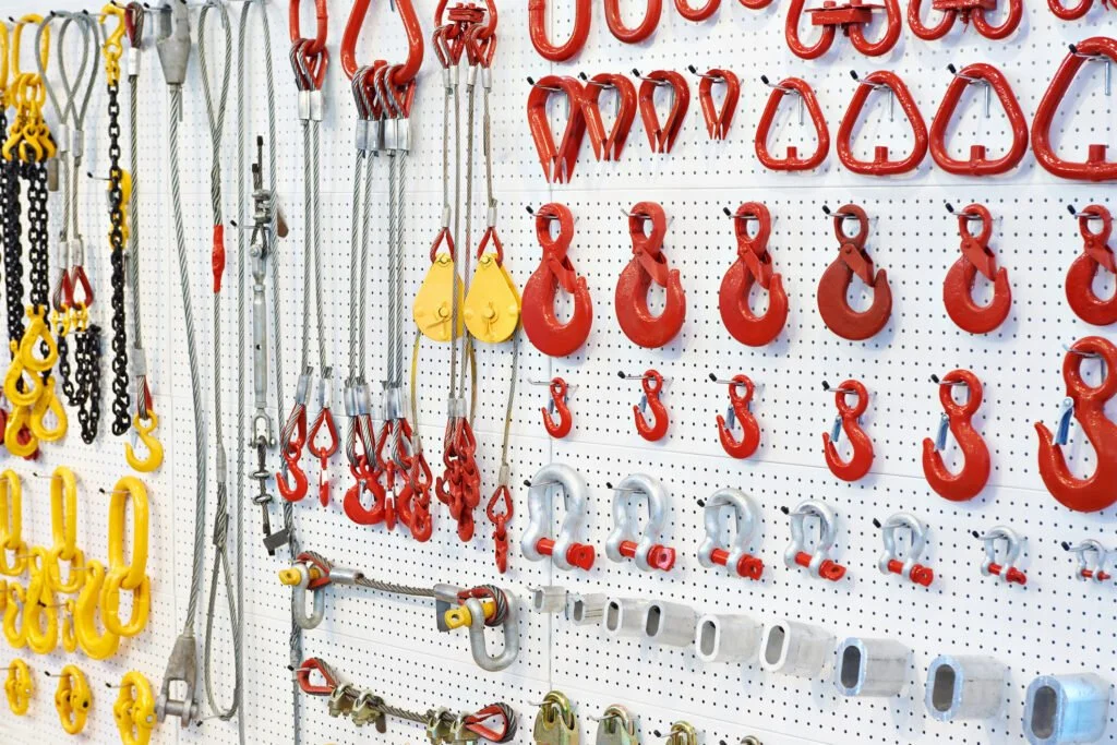 Ganci e catene di sollevamento rossi, gialli e argentati appesi su una parete forata in un negozio di attrezzature industriali di TSC S.r.l.