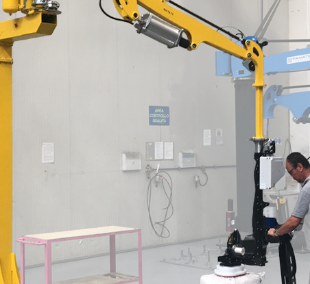 Un robot industriale con bracci articolati di colore giallo e blu che lavora in un laboratorio o centro di controllo, con un uomo che opera il robot e un tavolo senza oggetti.