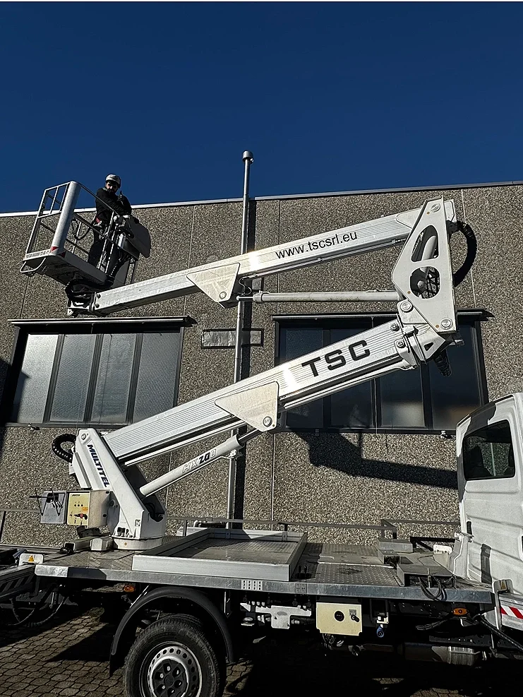 Un operaio su una piattaforma elevatrice sta lavorando sulla facciata di un edificio moderno con finestra.