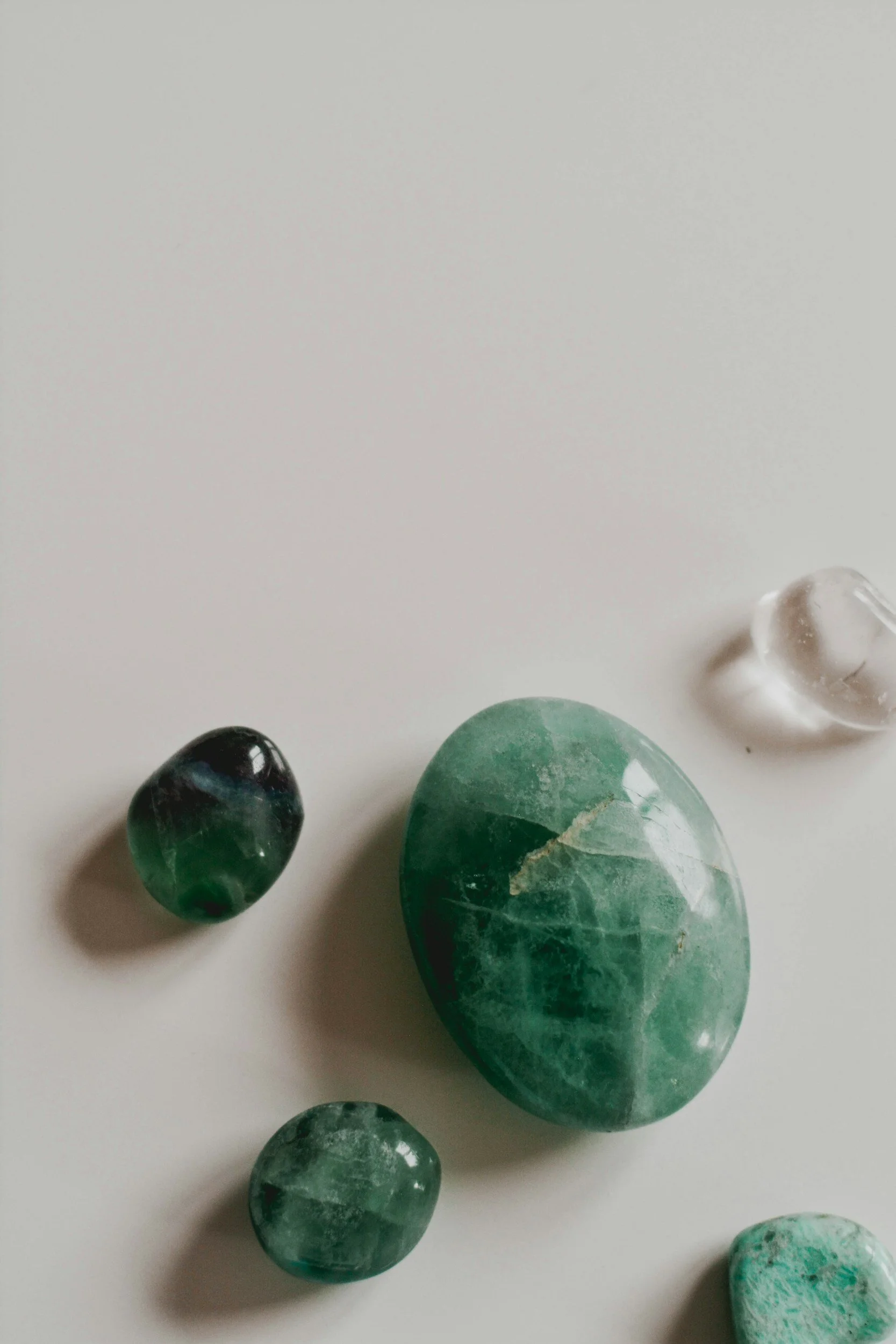 Several polished green and black stones and a clear quartz crystal on a white surface.