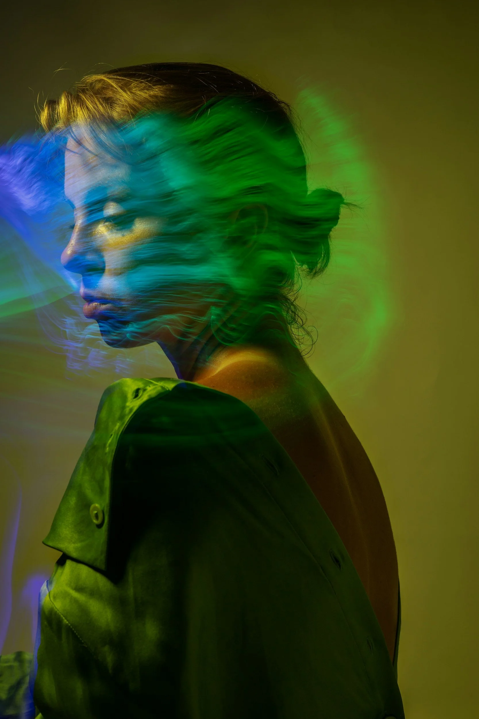 Profile of a woman with her hair pulled back, wearing a green trench coat, with colorful light streaks across her face and background.