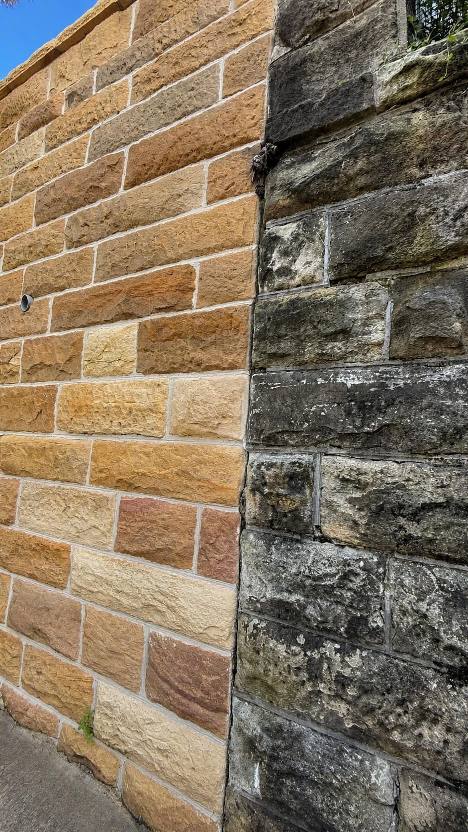 Close-up view of a brick wall with two distinct textures and colors: a section of smooth, reddish-brown bricks on the left and darker, rougher, weathered stones on the right.