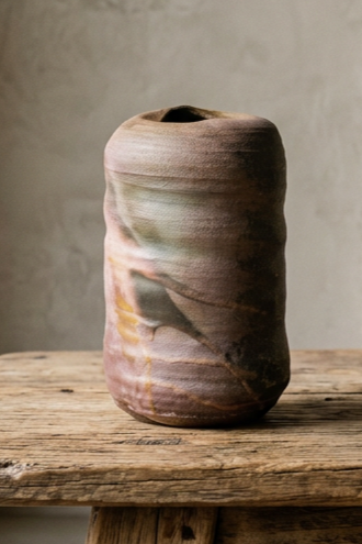 A ceramic vase with a marbled, multicolored finish placed on a rustic wooden surface against a plain, light-colored wall.