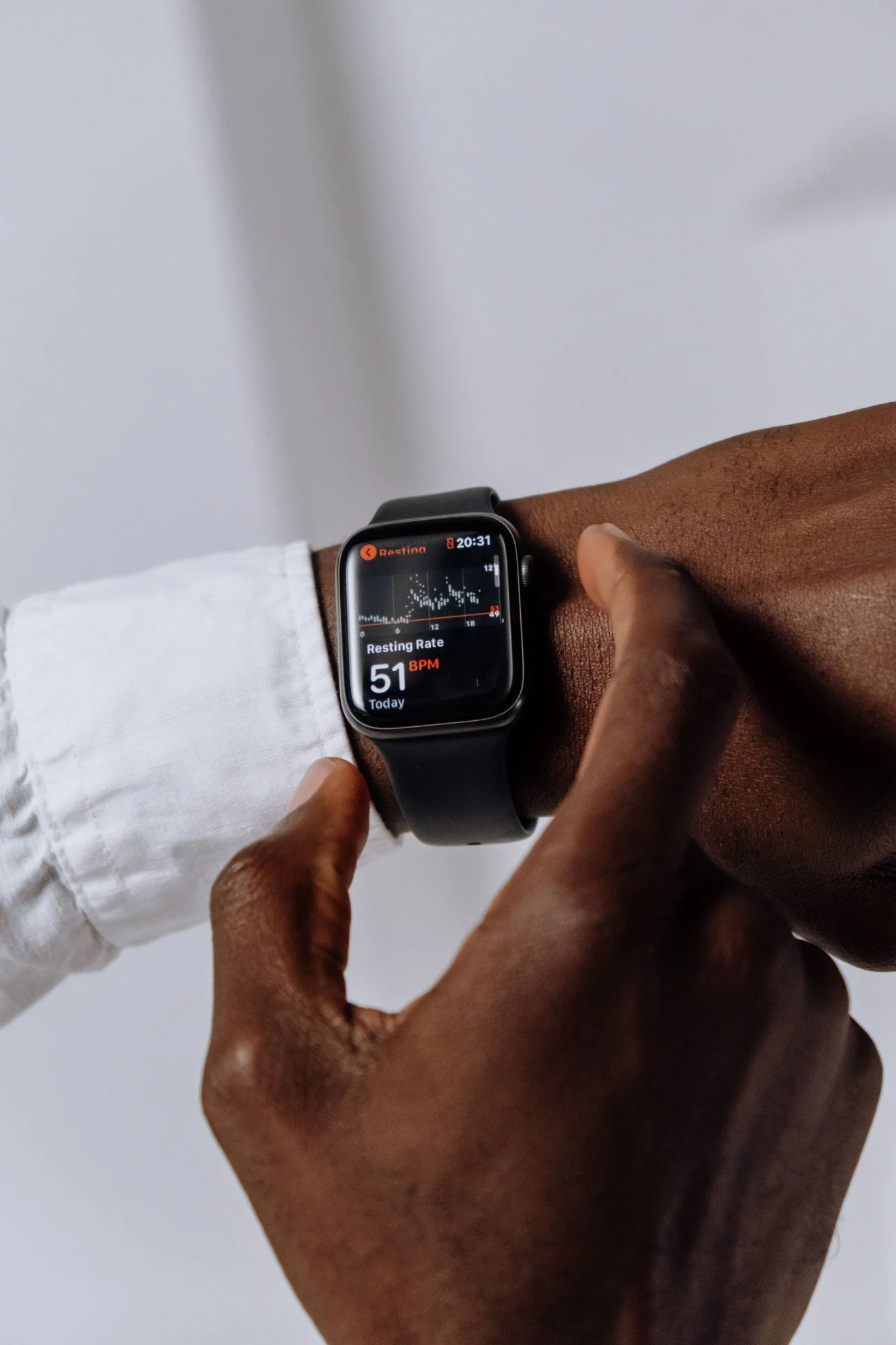 Close-up of a person's wrist wearing a smartwatch displaying a resting heart rate of 51 bpm. Two hands, one darker-skinned and one lighter-skinned, are touching the wrist.