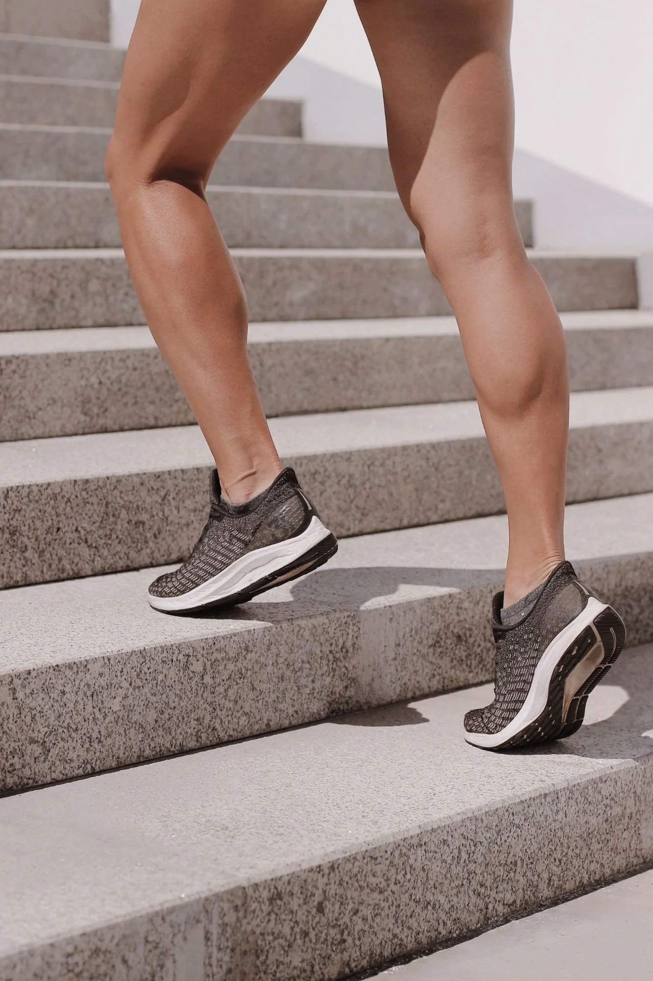 Person wearing gray athletic shoes climbing stairs made of gray concrete.