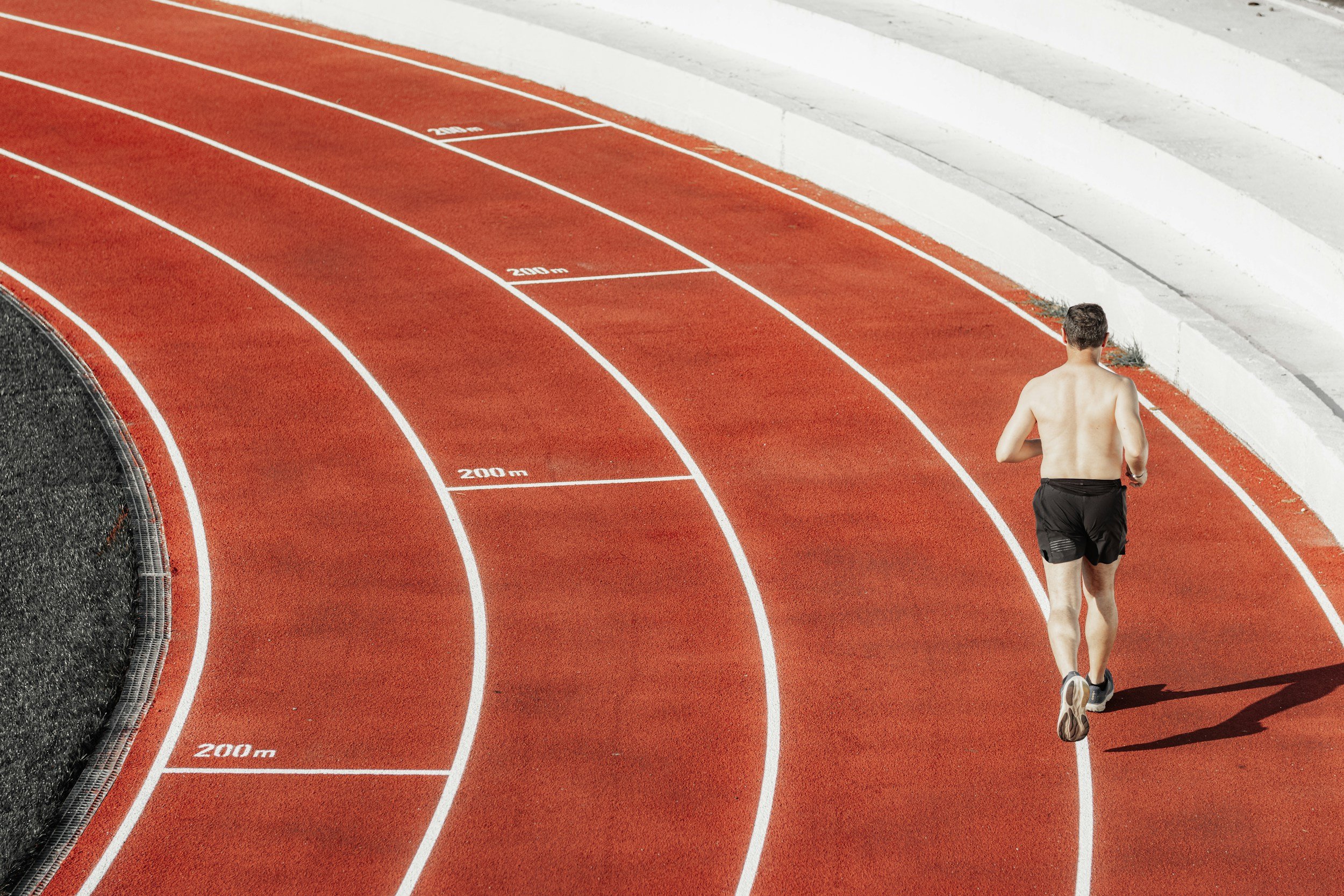 A man running on a red athletic track with white lane markings, next to a concrete wall and a black edge on the left side.