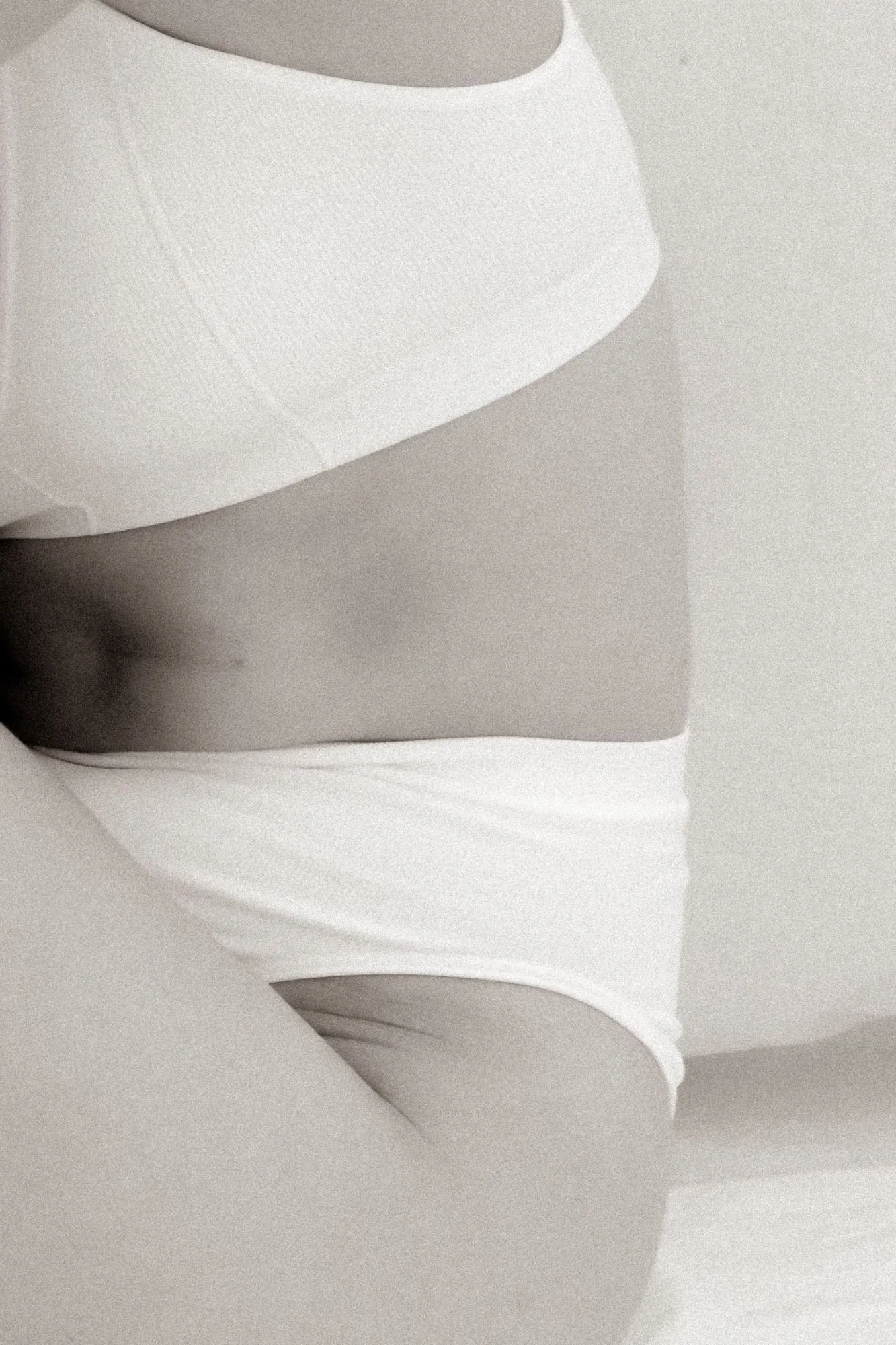 Close-up view of a woman in white underwear, with part of her body and the wall behind her visible.