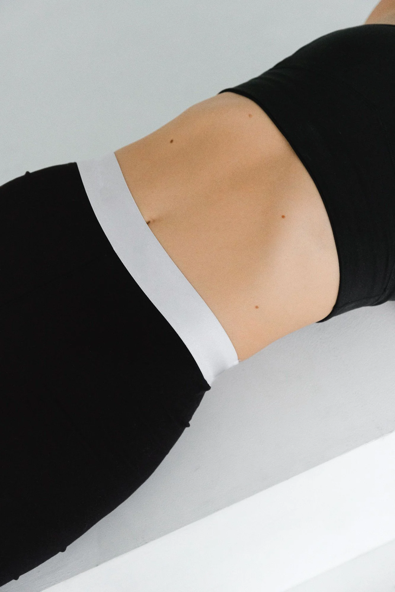Close-up of a person’s midsection wearing black pants and a white top, with a white background.