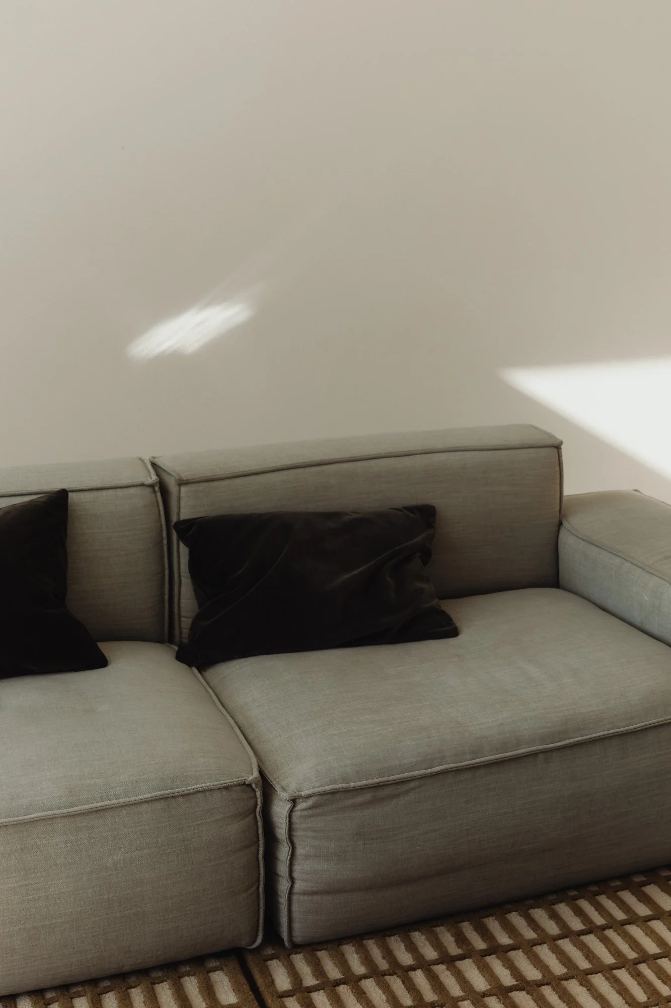 A beige sectional sofa with black cushions on a patterned rug.