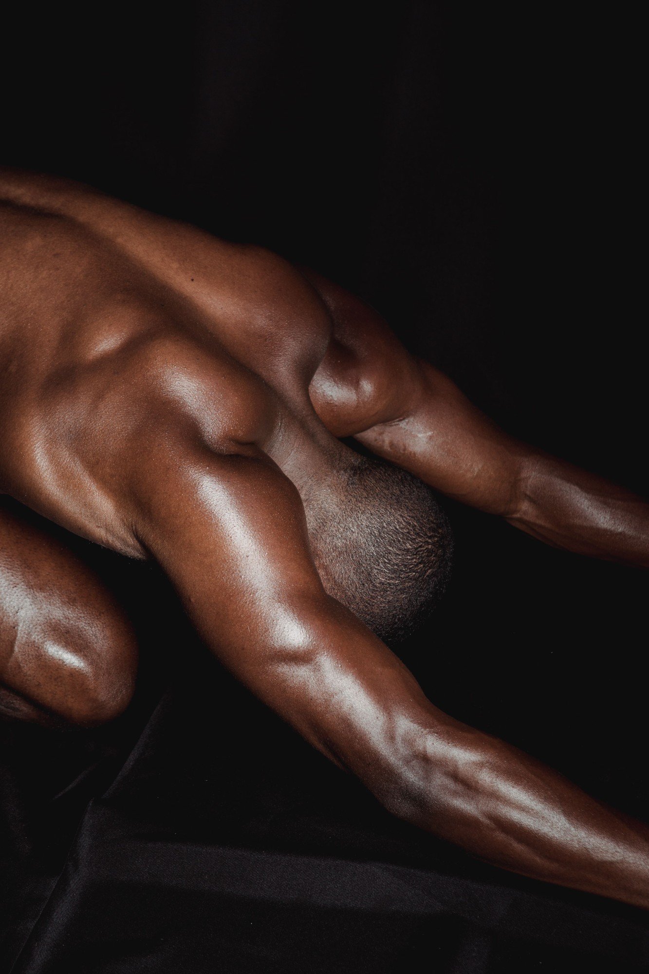 Close-up of the intertwined arm and shoulder of a person with dark skin against a black background.
