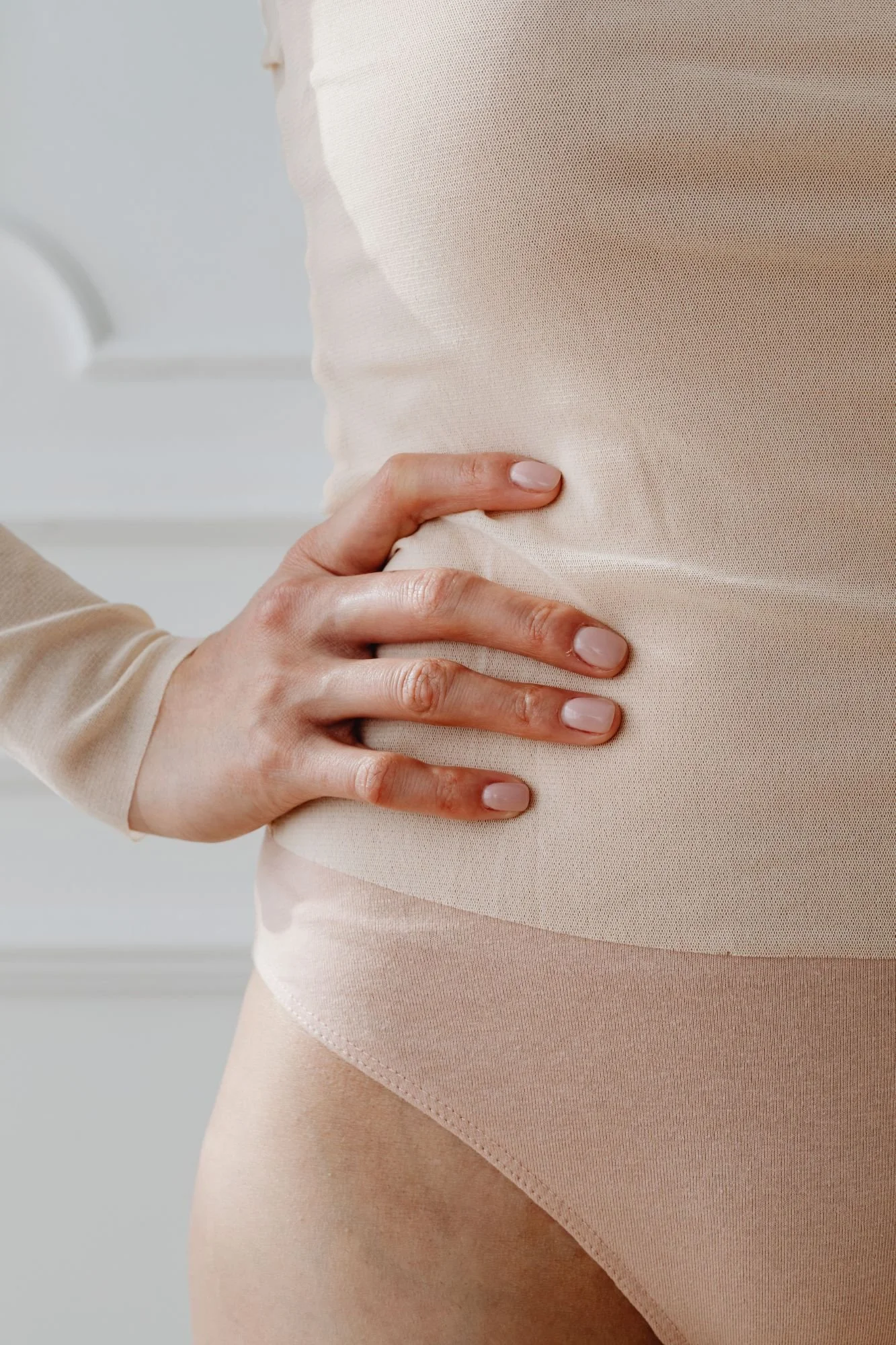 A person wearing beige undergarments and a beige top, with one hand resting on their hip.