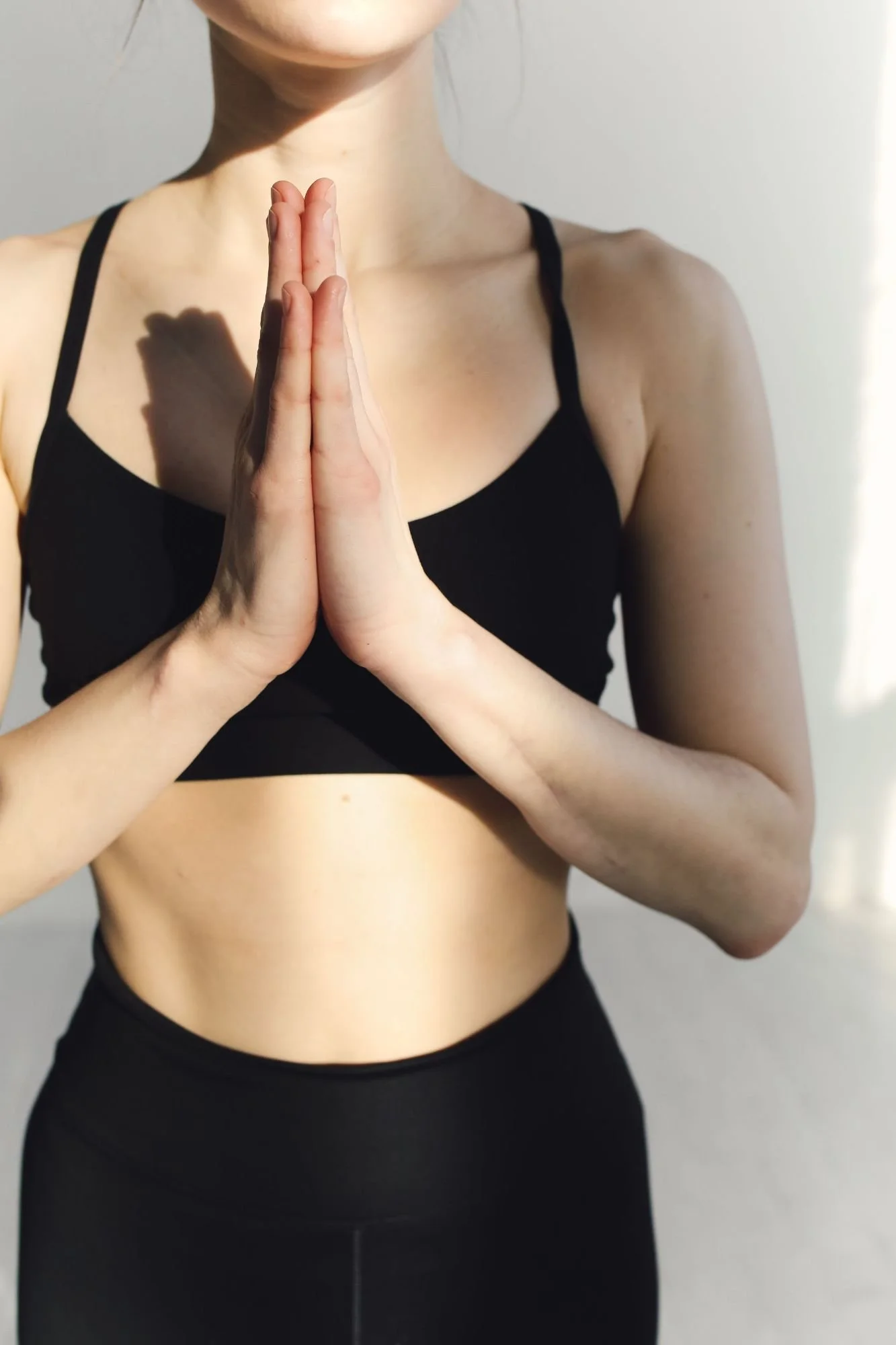 A person practicing yoga, standing with hands in a prayer pose against a plain background.