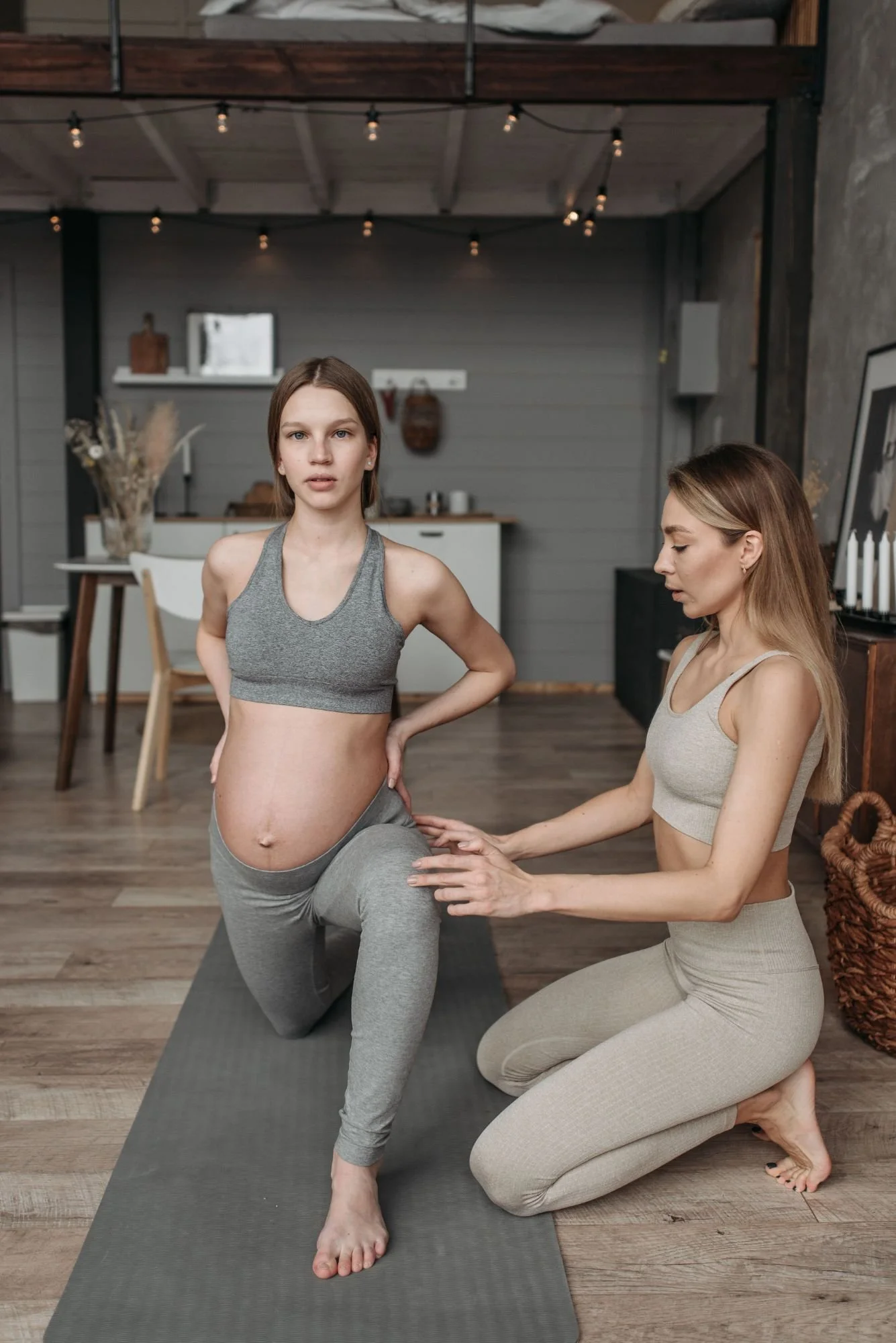 A pregnant woman practicing yoga with assistance from an instructor in a cozy home setting, with wooden floors and modern decor.