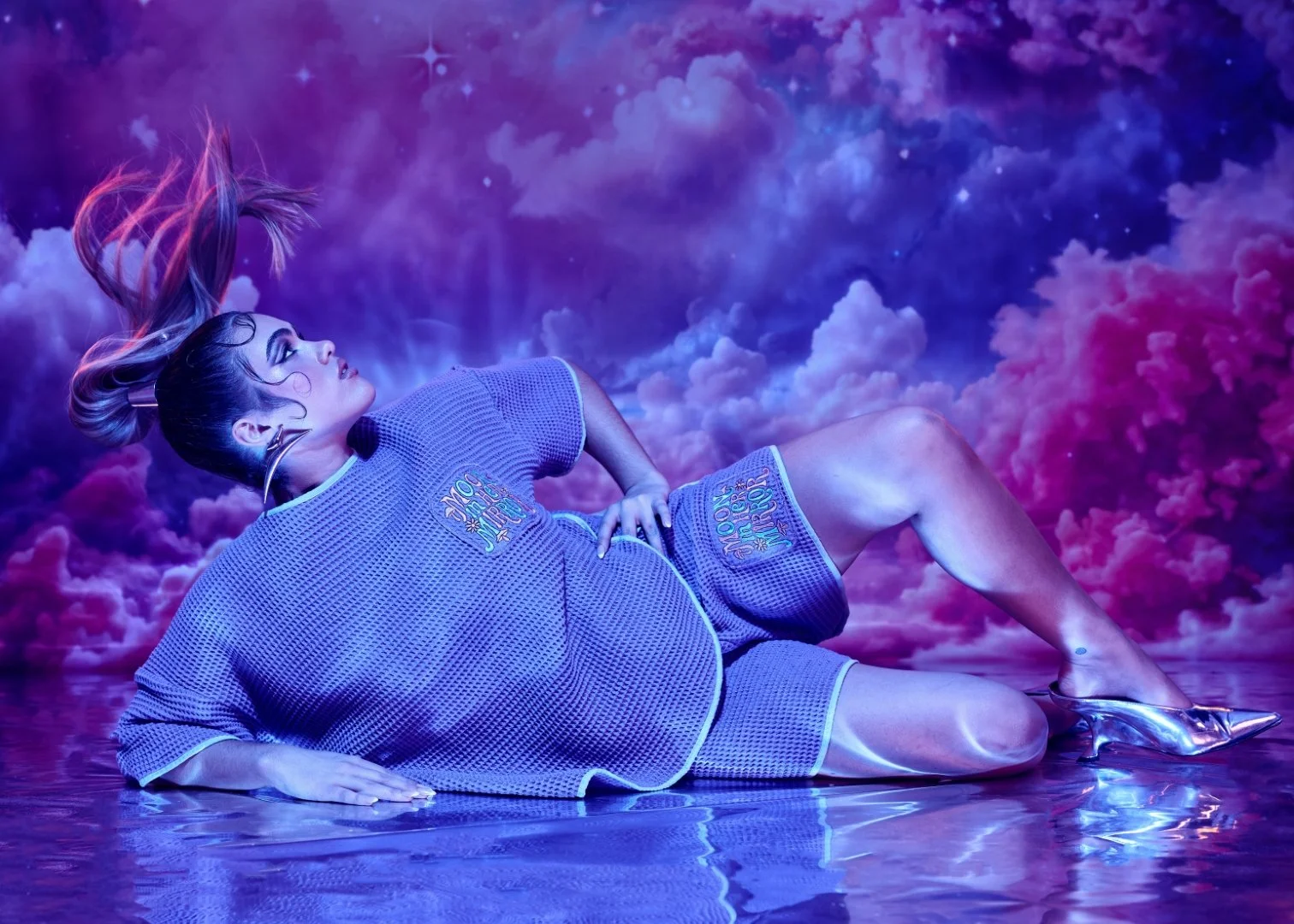 A woman with long hair floating over a metallic silver chrome floor, surrounded by a purple and pink nebula sky backdrop, wearing a purple top and shorts with metallic silver chrome high heels.