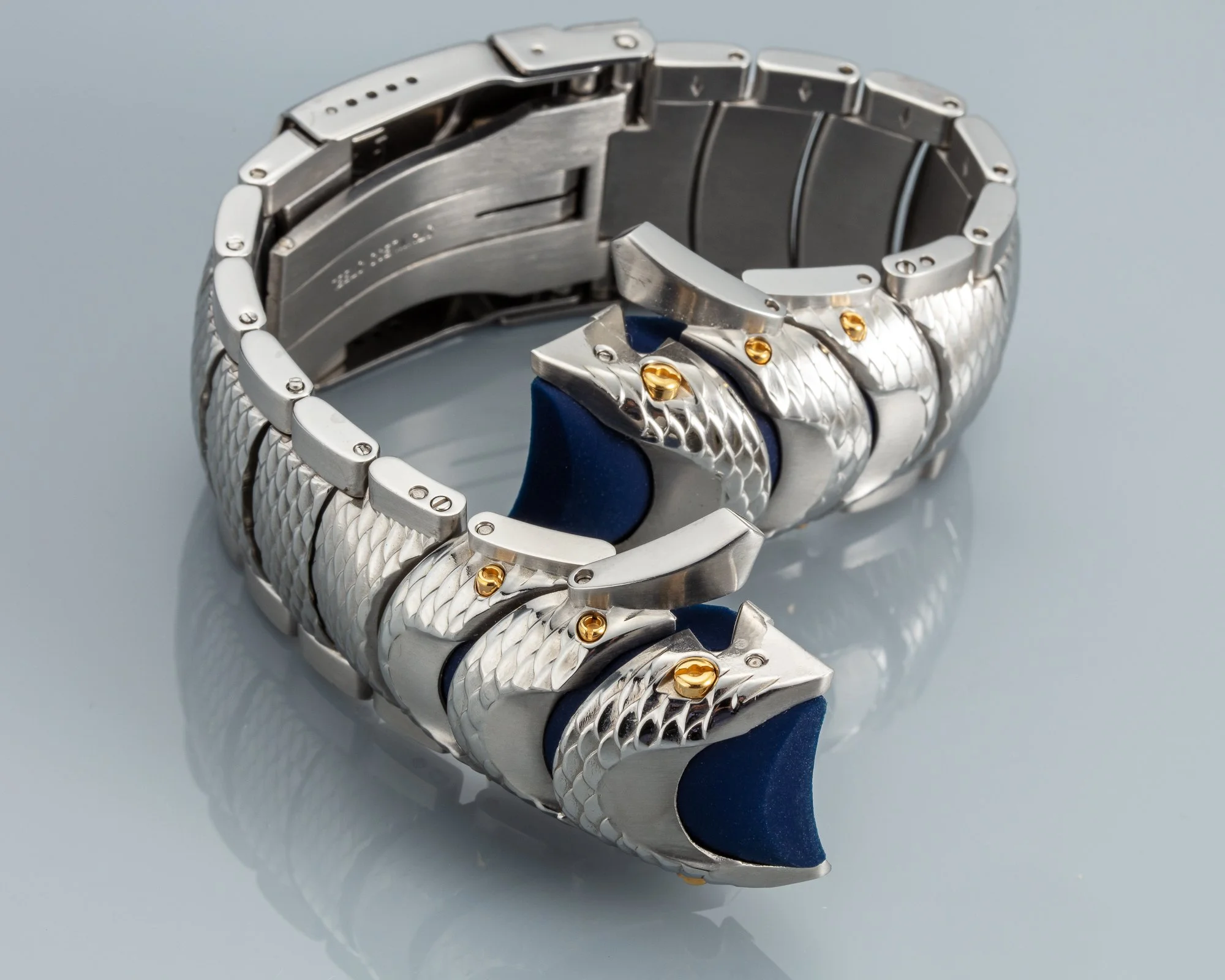 A silver metal watch with a textured band, partially open with blue and gold accents visible.