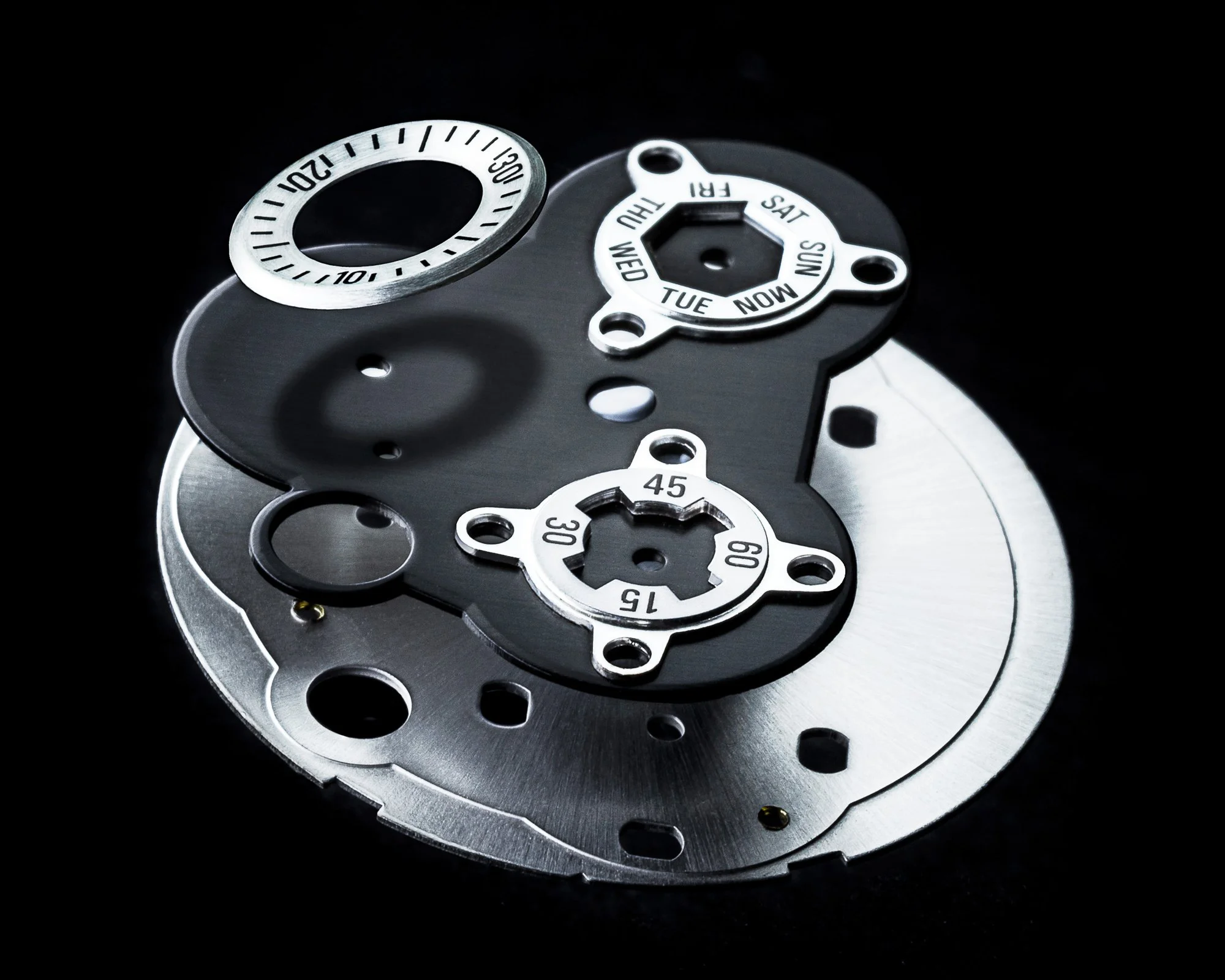 Close-up of a mechanical watch movement, showing gears and date and day dials on a black background.