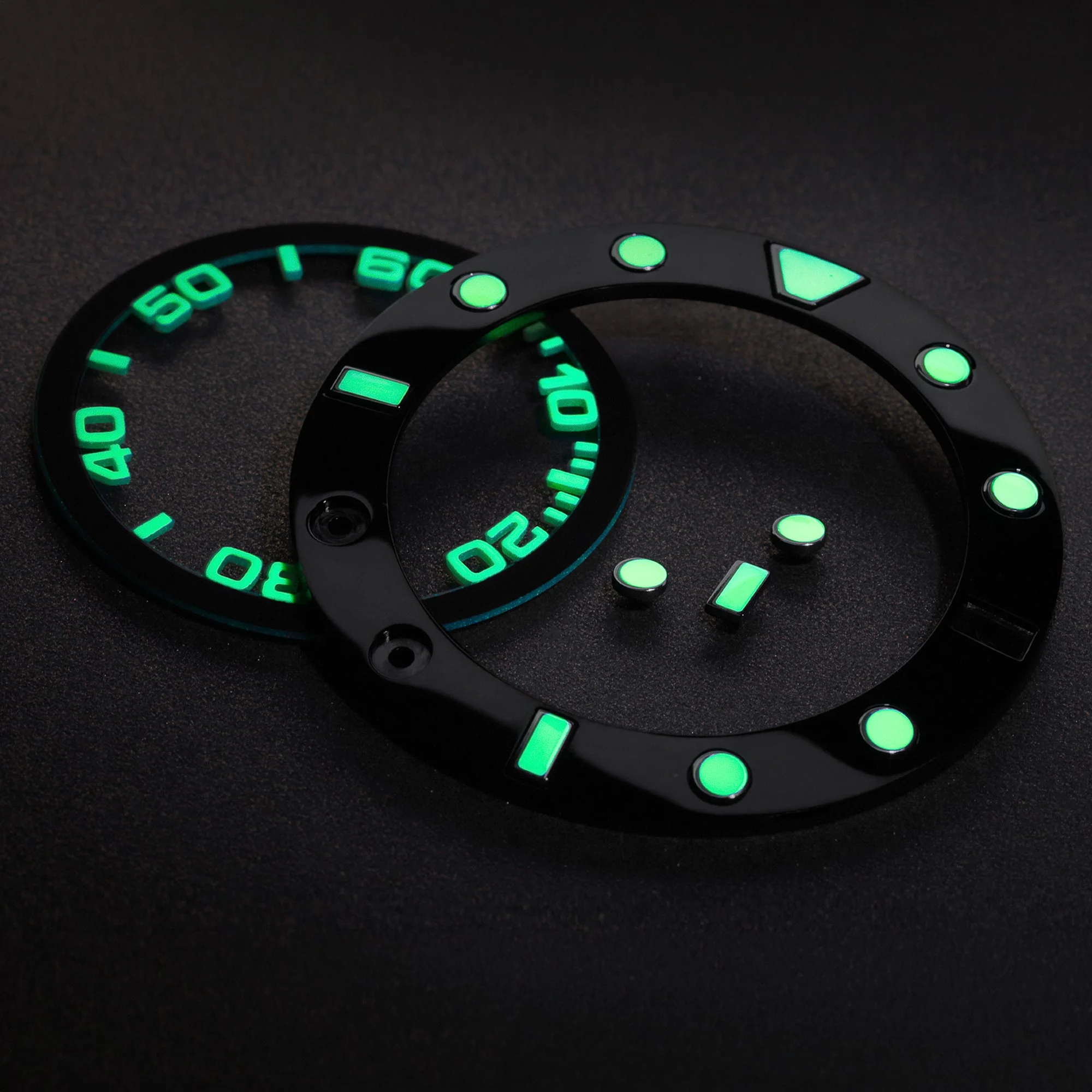 Close-up of a black diver's watch bezel with luminescent green markings and a triangle indicator against a dark background.