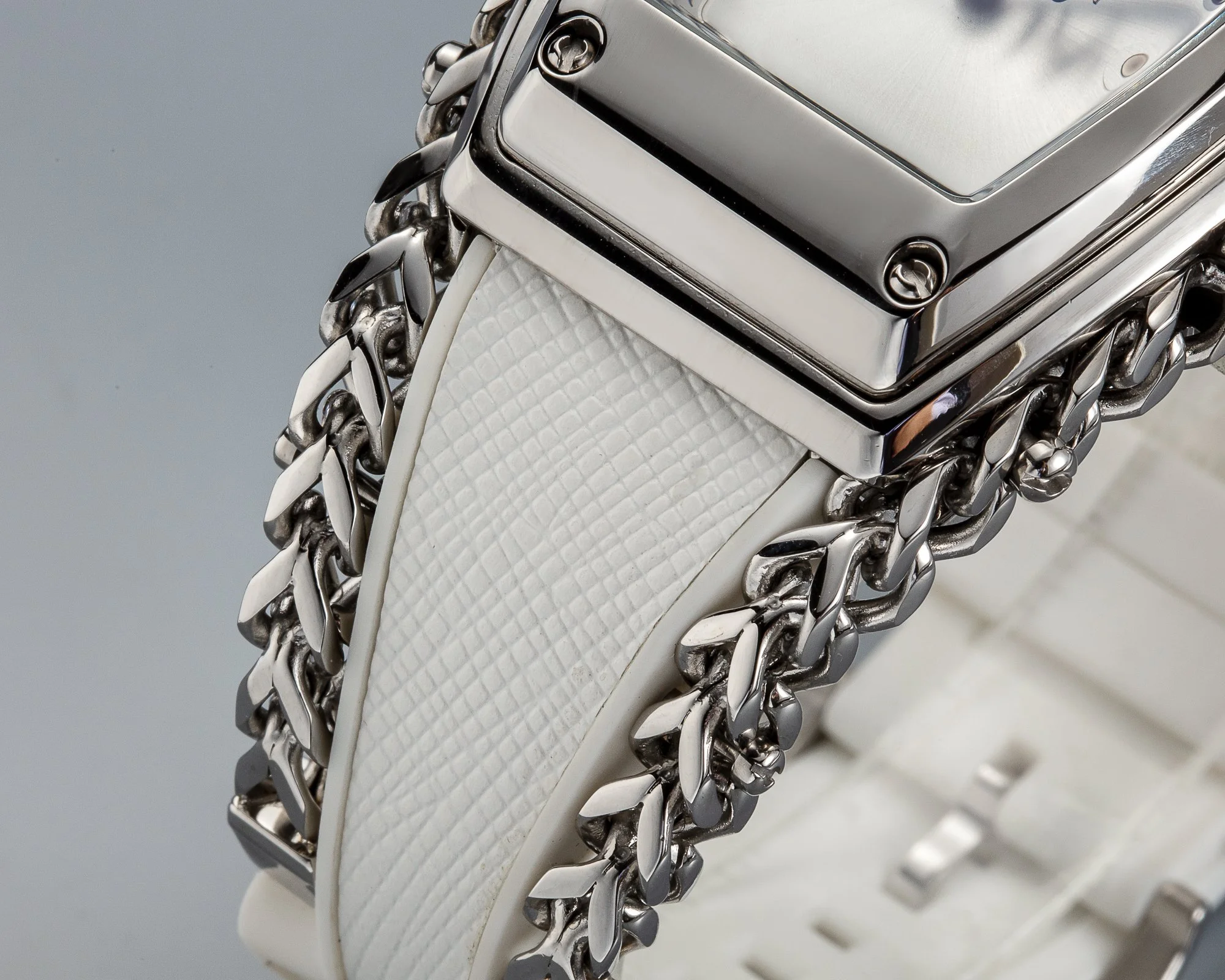 Close-up of a silver watch with a white textured band and silver chain links around the bracelet.