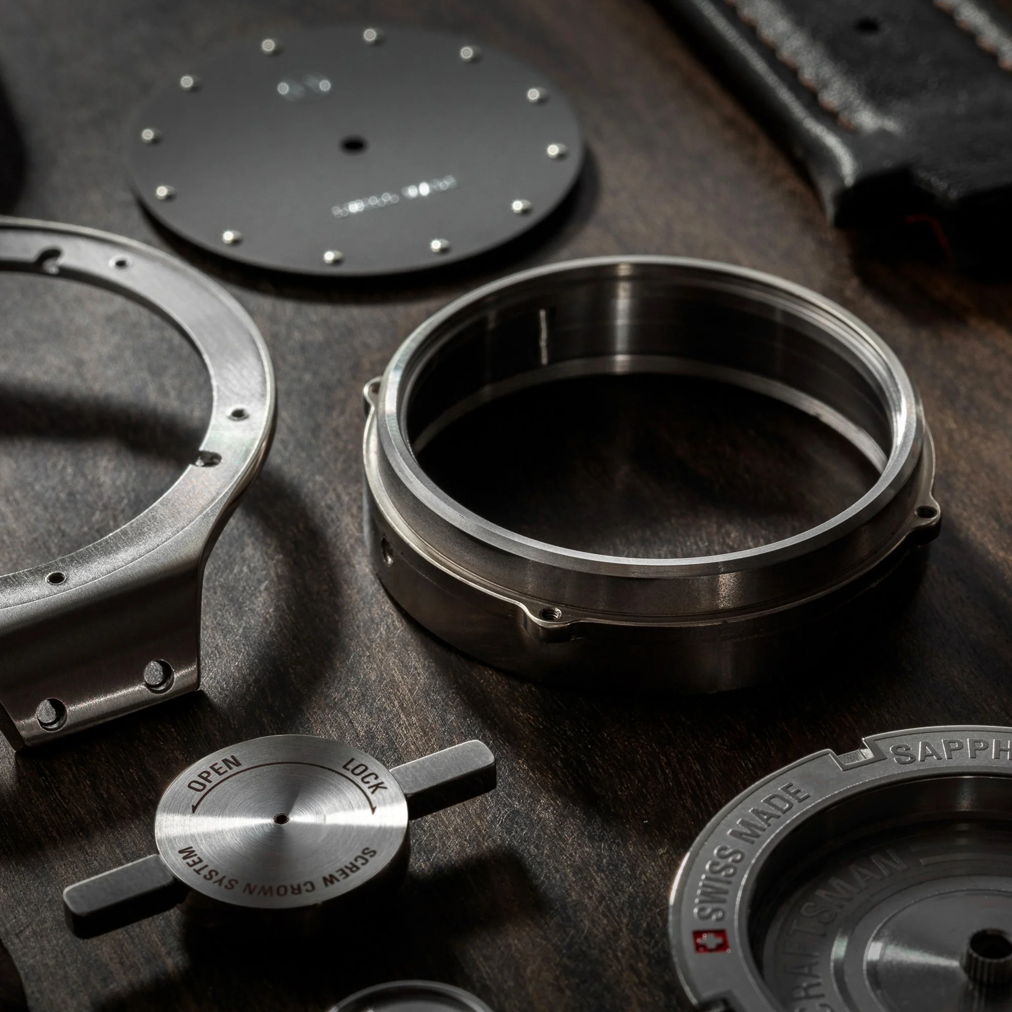 Close-up of metallic precision-machined circular parts with engraved text and markings, including a dial labeled "SWISS MADE" and other components with screw holes.